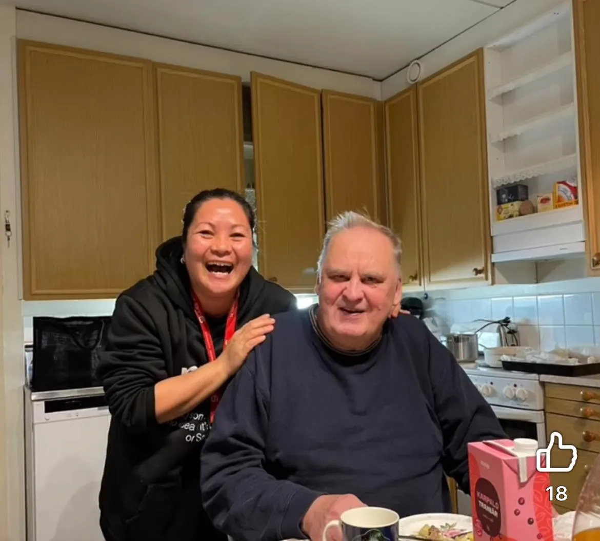 Nainen ja vanhempi mies hymyilevät keittiössä pöydän ääressä istuen.